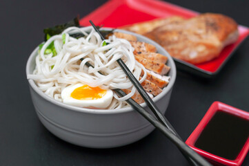 Ramen noodles are wrapped on chopsticks on a plate - a national, popular dish of traditional Japanese cuisine. Asian soup with wheat noodles, chicken breast, egg and broth.