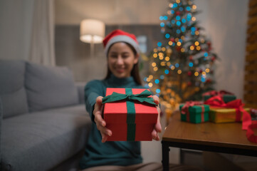 Obraz na płótnie Canvas Happy smiling young Asian woman in santa claus hat showing gift box to camera