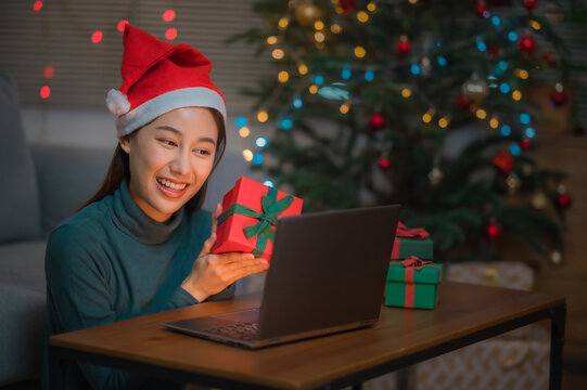 Happy Asian woman showing presents gift box to camera on laptop during chirstmas or new year holidays. Online celebration at home