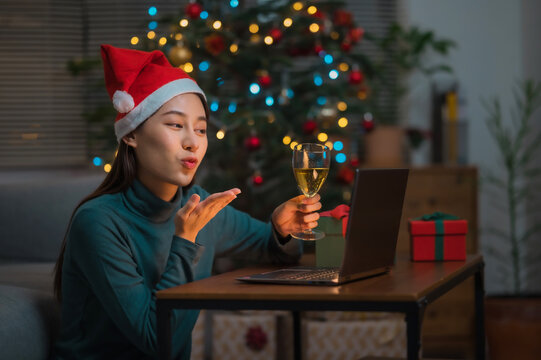 Asian woman wearing Christmas hat drinking champagne video call celebrate Happy New Year party online with her friends or family via laptop at home