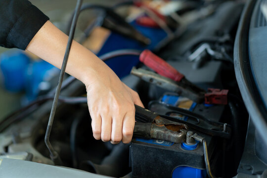 Asian Young Woman Holding A Tablet On Her Hand And Inspecting An Old Vehicle Battery, Woman Recharge A Car Battery From Other Battery. Asian Woman Fixing Her Car Herself.