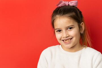 Portrait of happy joyful small caucasian girl in front of red background looking to the camera with...