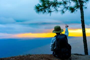 traveler backpacker on a hill, enjoying the panorama of mountain peaks and pointing the sun in the evening sky at sunset