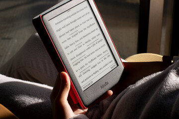 Fototapeta premium Portland, OR, USA - Dec 5, 2021: A girl reads Harry Potter from her Kindle in the afternoon sun.
