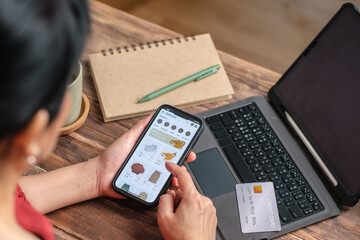 close up woman hand using credit card shopping online on mobile app on wood table at home
