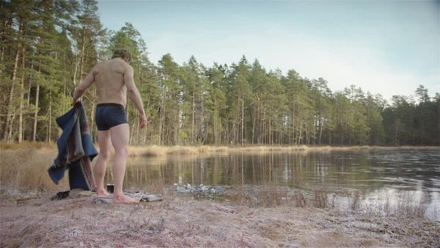 A fit muscular ice bather removes his poncho and prepares to enter the frozen lake