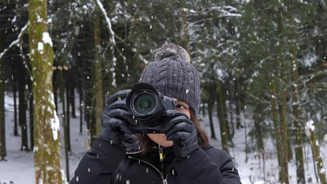Attractive woman taking pictures of winter forest during snowfall, static view