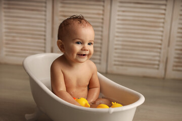 a baby of 11 months is bathing in a white baby bath with rubber ducklings, the baby is laughing, the concept of children's goods. high-quality photography