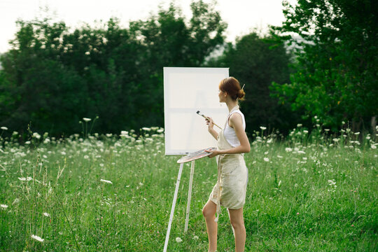 woman artist paints on easel in nature landscape
