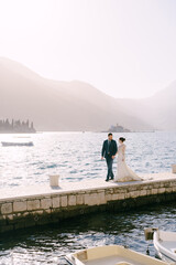 Bride and groom walk along the pier against the backdrop of the islands near Perast. Montenegro