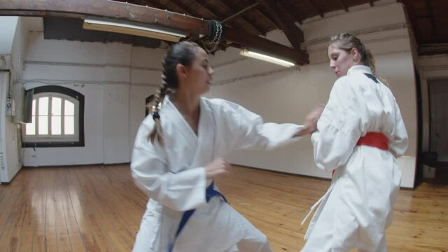 Handheld shot of focused karatekas fighting actively in gym. Side view of hard-breathing girls in kimonos training together, preparing for championship, improving skills. Martial arts, sport concept
