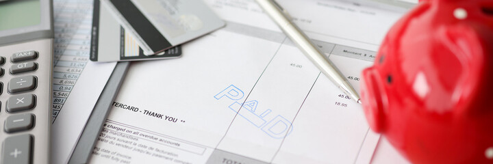Paid words and calculator with a piggy bank on counting paper for payment closeup