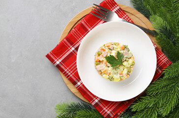 Olivier salad in a white plate on red textiles among spruce branches on a gray concrete background. A traditional Russian dish for Christmas and New Year. Top view. Copy space.