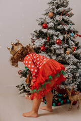 little curly-haired girl in a red carnival dress is looking for a Christmas gift under the Christmas tree. child is happy with the gift. lifestyle, children's emotions. High quality photo