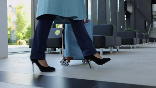 Close-up of businesswoman holding suitcase and walking in airport, waiting for flight spbi. Foot view of young woman traveler moves luggage in her hand and walks in light interior, waits for departure