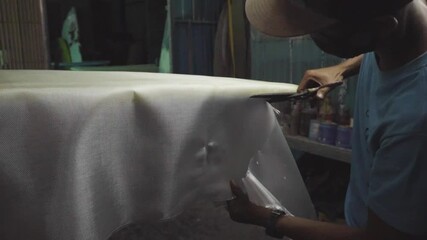 A man cutting a fiberglass cloth that is applied on a surfboard during glassing process. - Powered by Adobe