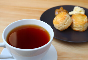 Closeup a cup of hot tea with blurry plate of scones in the backdrop