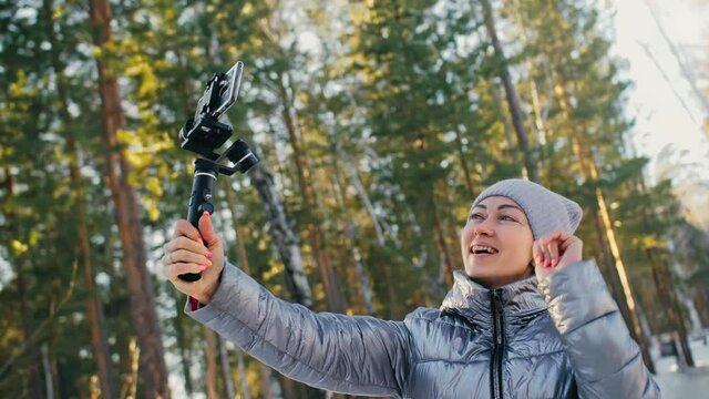 Woman Holding On Handheld Film 3-axis Gimbal Stabilization Device in Winter for Smartphone. Videographer Operator Take Photo Video.