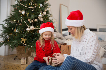 mom and child daughter in a Santa's hat with Christmas presents at home near the Christmas tree. family meets Christmas together at home. family traditions to celebrate Christmas