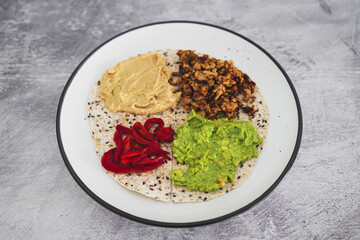 plant-based food, vegan version of the viral layered tortilla wrap hack with red peppers hummus avocado and shredded teriyaki tofu