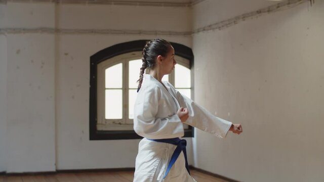 Tracking shot of focused girl performing karate movements. Long shot of concentrated beautiful Caucasian teenager learning karate poses in gym, devoting time to hobby. martial arts, sport concept