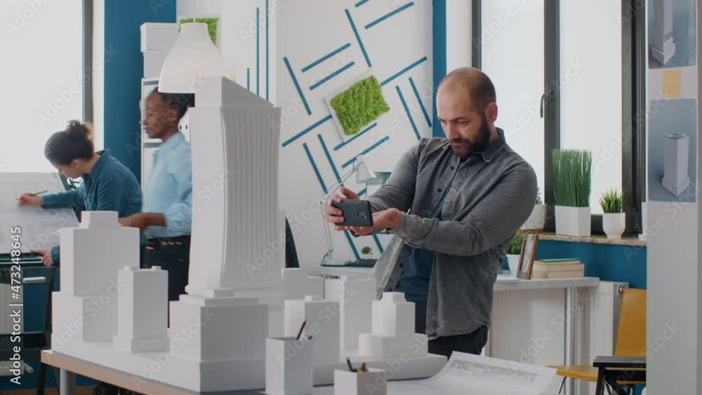 Poster man engineer using smartphone to work on building model and layout in architectural office. architec