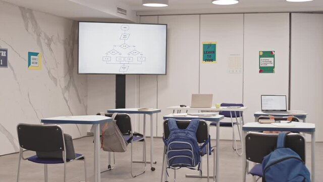 Tracking Right View Of Classroom With No People In, Backpacks Hanging On Chairs, Notebooks, Laptop And Pens On Desks