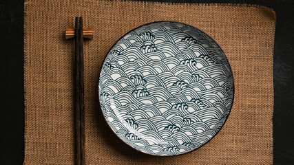 Ceramic plate with chopsticks on brown placemat.