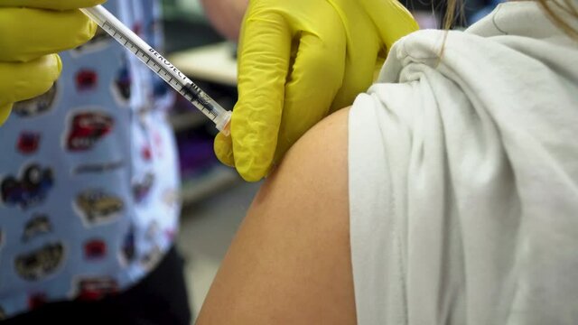 Medical Worker In Yellow Surgical Gloves Injecting A Dose Of Covid Vaccine Onto The Arm. close up
