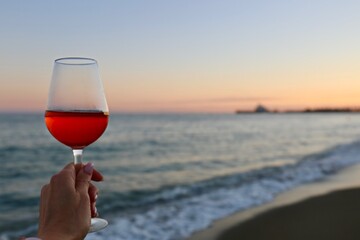 person holding a glass of red wine at sunset