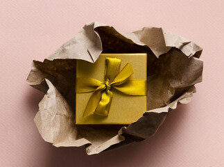 Gift box in craft paper on warm pink pastel background, scissors and wrapping paper nearby. The concept of preparing gifts for the holiday. Top view, copy space