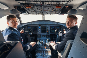 Two pilots sitting in cockpit and looking at camera - obrazy, fototapety, plakaty