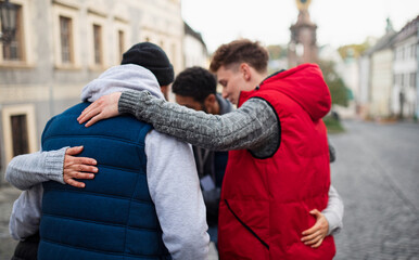 Rear view of community service volunteers hugging together outdoors in street