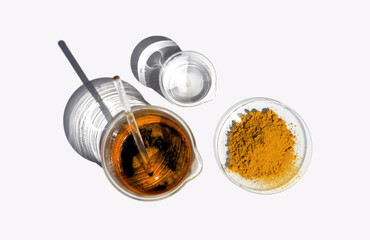 Organic Curcuma Powder in Chemical Watch Glass, Ferric Chloride Liquid with stirring rod and Crystal clear liquid in Beaker. Closeup chemical ingredient on white laboratory table. Top View