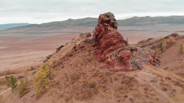 Flying around the cliff sightseeing. Red sandstone protrudes from the mountain. Autumn. Evening light in Khakassia. Autumn trees. Rock grandfather Ded Kazanovka