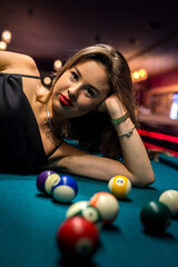 Beautiful woman in elegant black dress lying on the billiard table