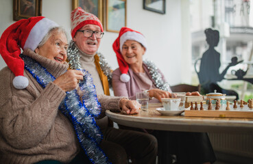 Happy senior friends sitting indoors in community center and celebrating Christmas.