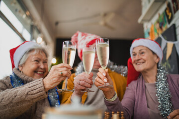 Happy senior friends sitting indoors in cafe clinking champagne glasses and celebrating Christmas.