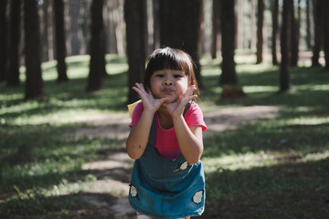 Fototapeta premium Active little girls running in the pine forest on a warm summer day. Happy girl smiles and laughs while spending time with her family in the park on vacation.