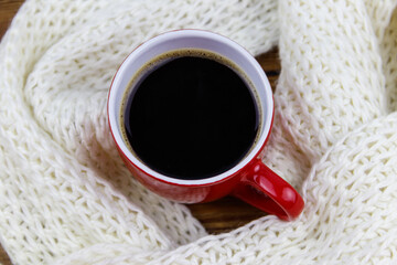 Obraz na płótnie Canvas Cup of coffee with white knitted scarf around it. Top view. Winter cozy concept