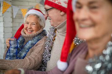 Happy senior friends sitting indoors in community center and celebrating Christmas.