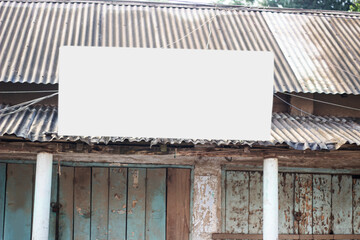 An old tin fence has a white blank board and its background is blurred.