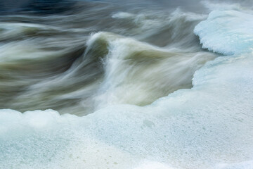 Long exposure shot of fast flowing wintry river with ice banks - obrazy, fototapety, plakaty