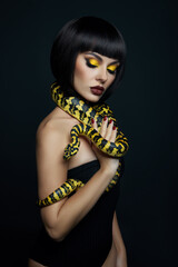 Beauty woman short haircut python yellow snake on her neck. A yellow snake on the shoulders of a girl. Beauty yellow eye shadow makeup, dark burgundy lipstick