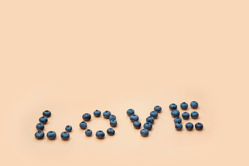 blueberries on a beige background. The word "love" is laid out with berries at the bottom of the frame