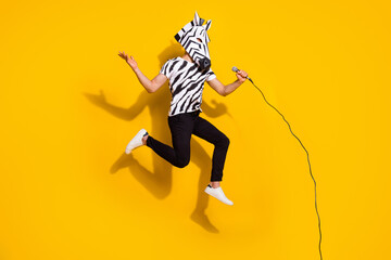 Fototapeta na wymiar Full length photo of crazy weird guy rocker in zebra mask jump up sing mic isolated over shine yellow color background