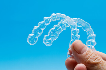Hand holding two transparent retainers on blue background. Invisalign orthodontics concept