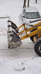 The front part of a bulldozer tractor engaged in clearing snow in a parking lot for cars