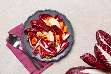 Apple, walnut, carrot and radicchio salad in a grey plate. Whole long radicchio. Top view, beige table surface.