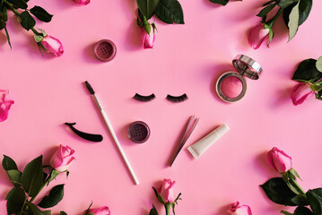 Fake eyelashes, tweezers, eyeshadows and lashes glue on pastel pink background with rose flowers. Fake lashes flat lay